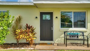 A house with a dark front door, a welcome bench, and a small garden with tropical plants. - Relax in Hot Tub, Walk to Springs: North Port Home (North Port)