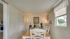 A dining area with a wooden table and white chairs, a potted plant, and wall-mounted lighting. - Relax in Hot Tub, Walk to Springs: North Port Home (North Port)