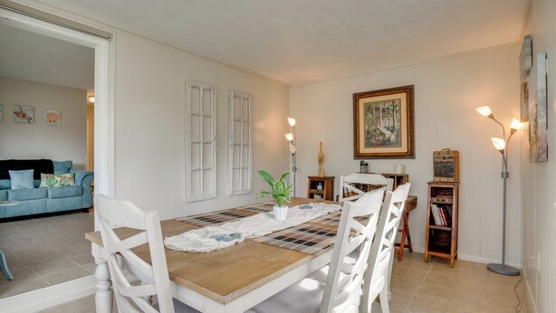 A dining area with a wooden table and white chairs, a potted plant, and a painting on the wall. - Relax in Hot Tub, Walk to Springs: North Port Home (North Port)