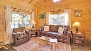 Ein gemütliches Holzhaus-Interieur mit Ledersofa, kleinem Tisch und einem Fenster mit Vorhängen.