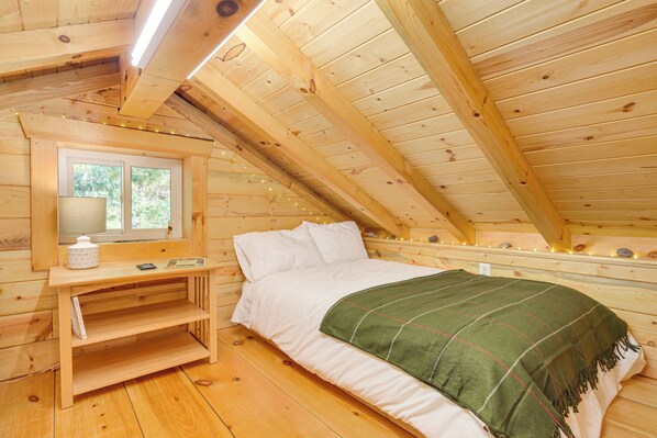 A wooden cabin room with a bed, a nightstand, a window, and a shelf. - Northwoods Nature Escape! Lakefront Hayward Cabin (Hayward)