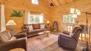 Ein gemütliches Blockhaus-Interieur mit Holzbalkendecke, einem Ledersofa, einem Liegesessel und einem kleinen Tisch.