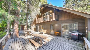 Una cabaña de madera con un porche, mesas de picnic y una parrilla.