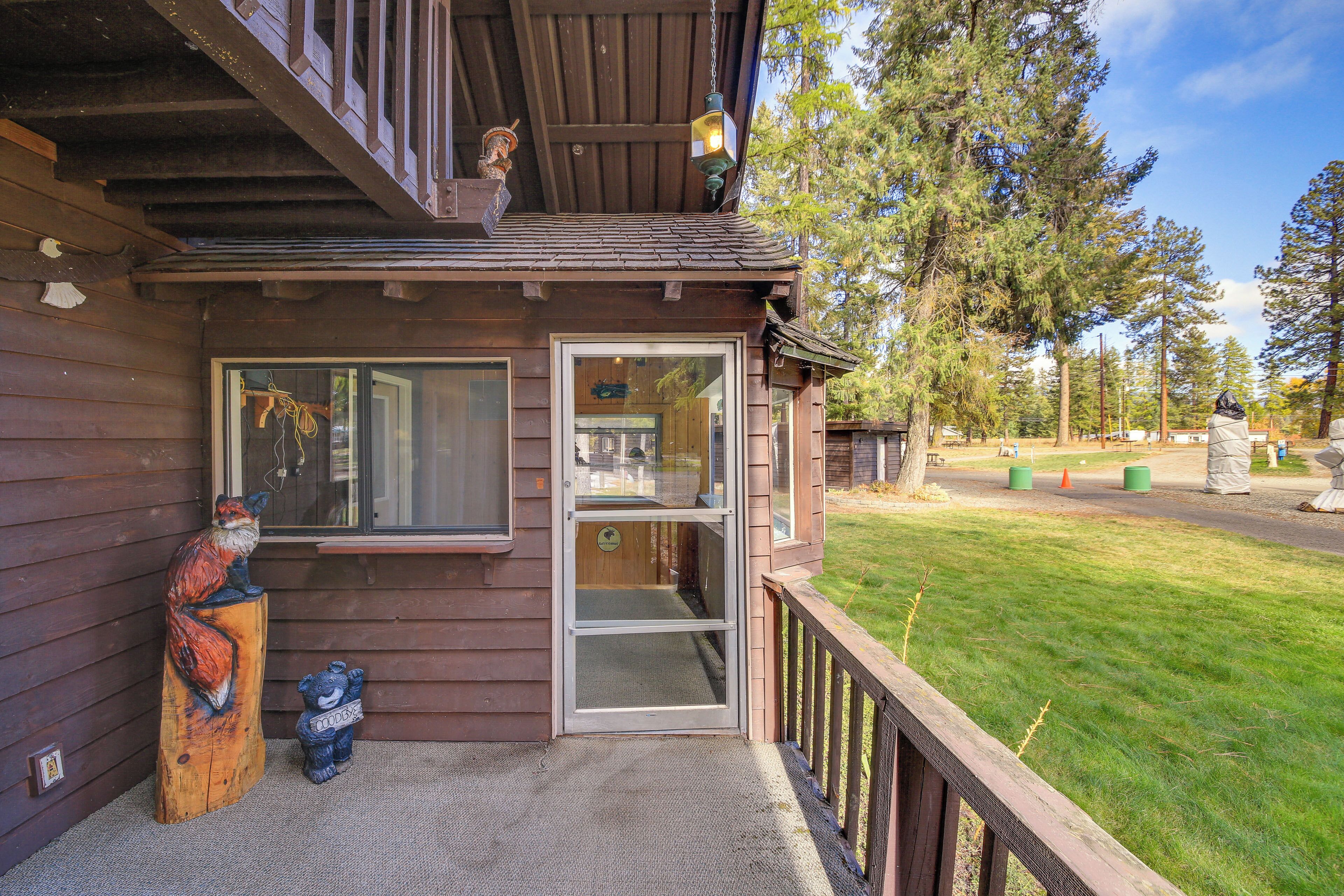 A wooden building with a glass door entrance, a wooden deck, and a bear statue on the left.