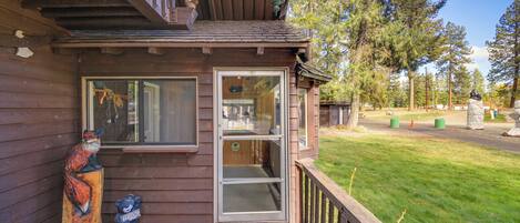 A wooden building with a glass door entrance, a wooden deck, and a bear statue on the left.