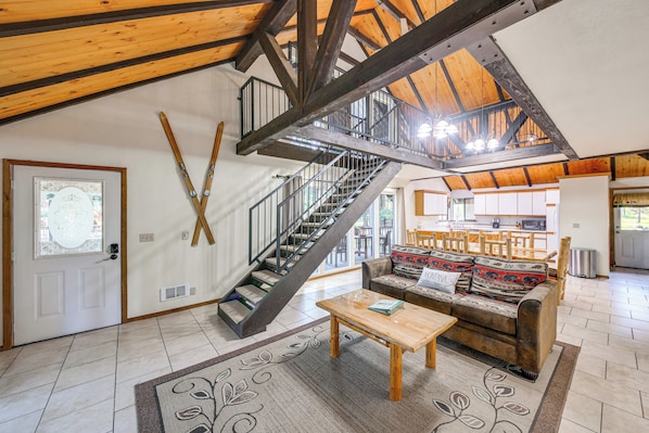 A spacious living area with a wooden staircase, a sofa, a coffee table, and a view of the kitchen in the background.