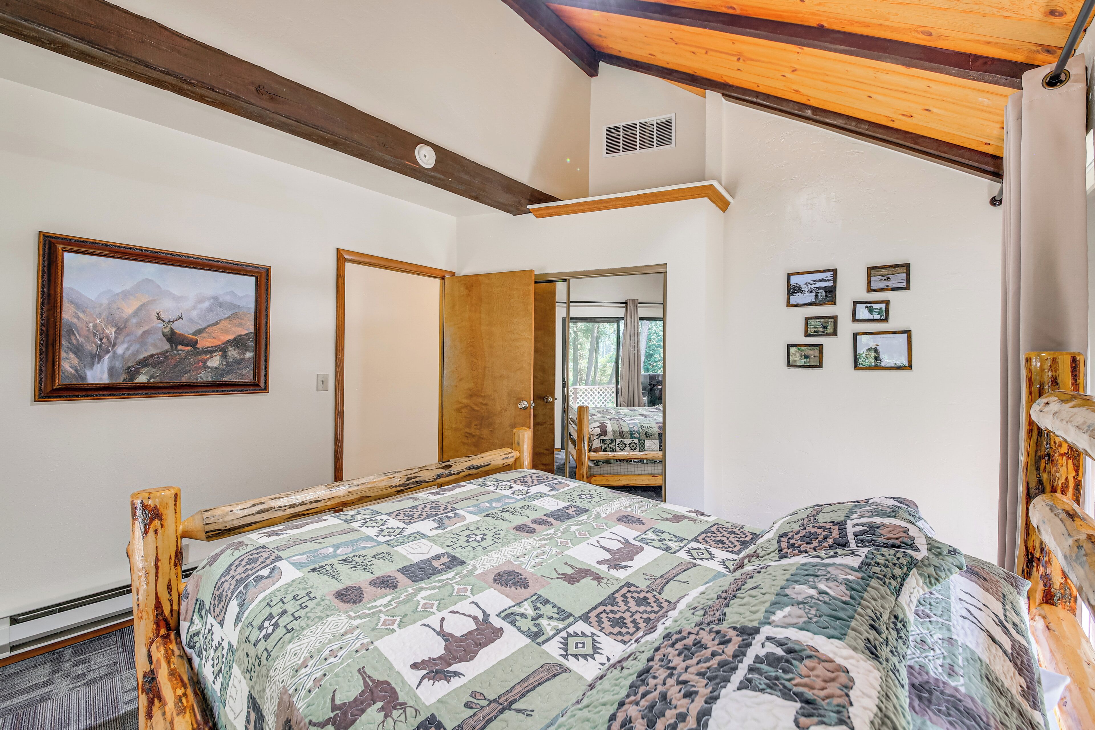 Un dormitorio con estructura de cama de madera, colcha con motivos de animales, un cuadro de paisaje montañoso y una puerta que da a otra habitación.