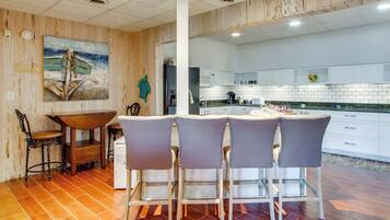 A modern kitchen with white cabinets, a central island with bar stools, and a wooden floor.