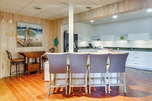 A modern kitchen with white cabinets, a central island with bar stools, and a wooden floor.