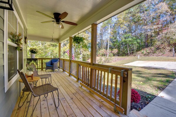 A covered porch with wooden flooring, a ceiling fan, and a view of a wooded area.