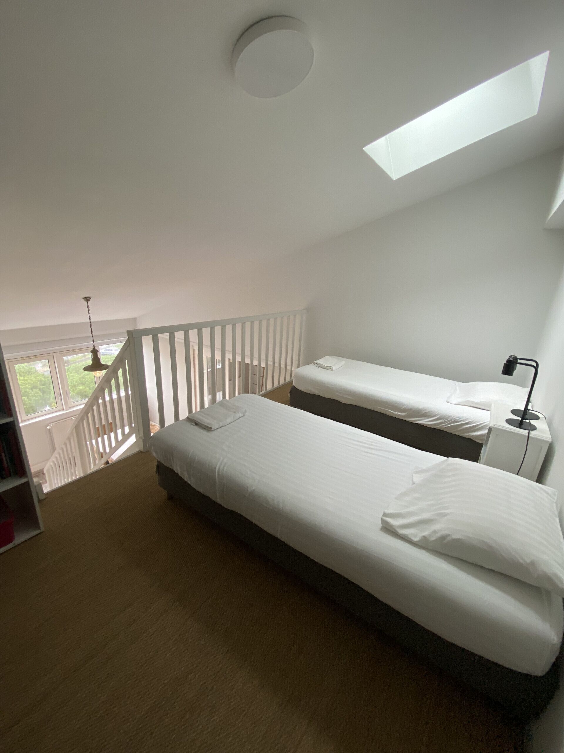 Une chambre avec deux lits, une lucarne, une rambarde blanche et une vue sur la verdure.
