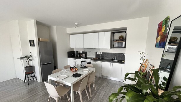 Une cuisine moderne avec des meubles blancs, une table à manger pour quatre personnes et un réfrigérateur.