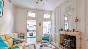 A spacious living room with a beige sofa, a blue armchair, a fireplace, and a kitchen visible through an open door.