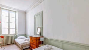 A bedroom with two single beds, a wooden dresser, a mirror, a radiator, and a window with a view.