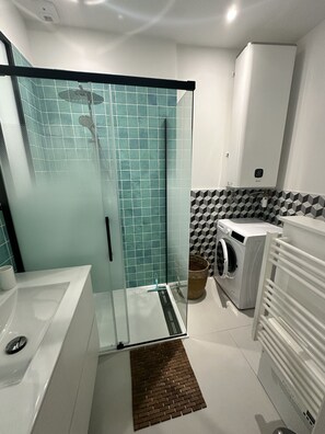 Ein modernes Badezimmer mit einer Duschkabine, einem weißen Waschbecken, einer Waschmaschine und einer gefliesten Rückwand.