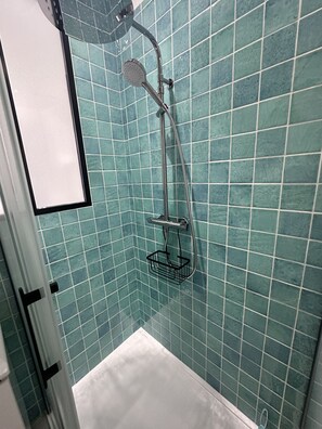 Ein Badezimmer mit Dusche, gefliesten Wänden und einer weißen Badewanne.