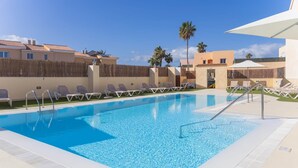Ein Pool mit Liegestühlen und Sonnenschirmen, umgeben von Gebäuden und Palmen.