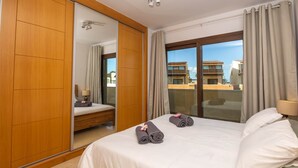 Ein Hotelzimmer mit einem großen Bett, einem Kleiderschrank, einem Spiegel und Blick auf Gebäude durch eine Glasdoor.