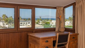 Ein Holztisch mit Stuhl, einer Vase und Blick auf eine Küstenlandschaft mit Gebäuden und Bergen.