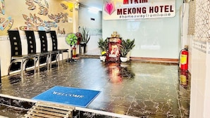 Aula, jossa on tervetulomatolla varustettu sisäänkäynti, vastaanottotiski, seinälle kiinnitetty kyltti, jossa lukee ”MYKIM MEKONG HOTEL”, sekä koristeellinen alttari, jossa on kasveja.