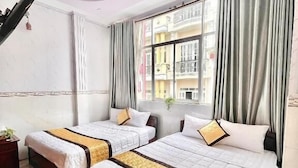 Hotellihuone, jossa on kaksi sänkyä, suuri ikkuna verhoilla, näkymä rakennuksiin ja puulattia.