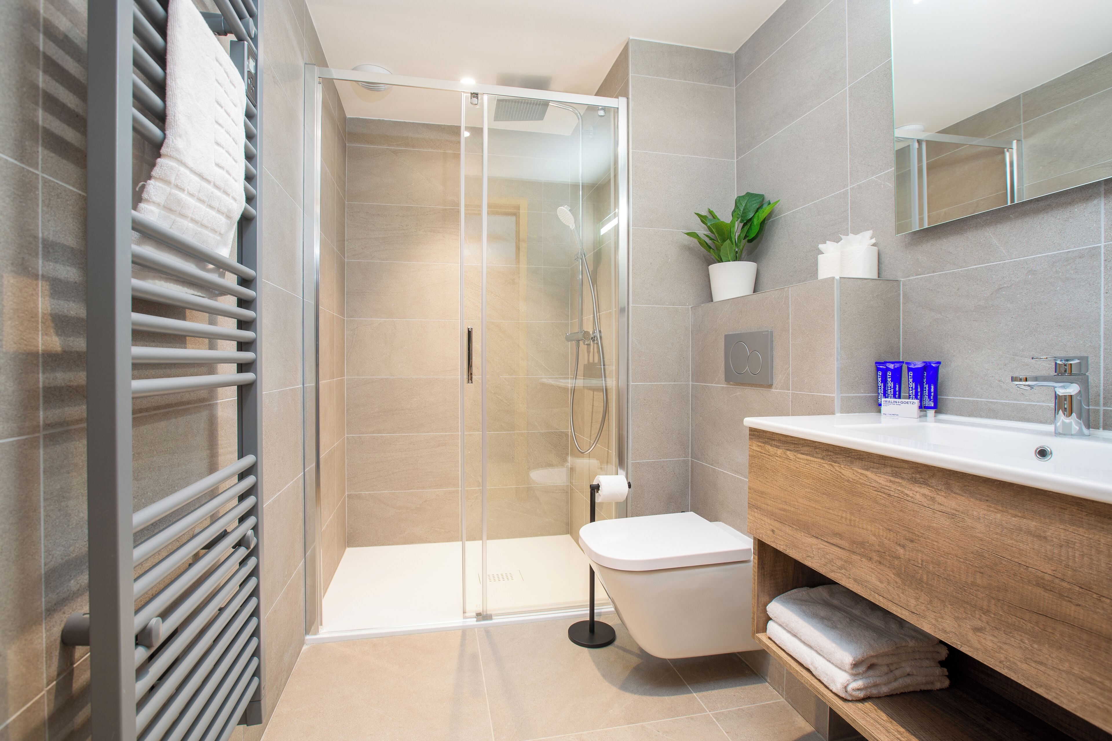 A modern bathroom with a glass-enclosed shower, a white toilet, a wooden vanity, and a potted plant.
