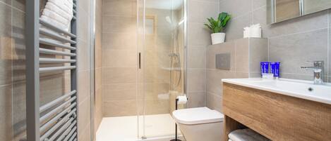 A modern bathroom with a glass-enclosed shower, a white toilet, a wooden vanity, and a potted plant.