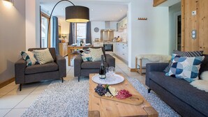 A modern living room with two sofas, a coffee table with snacks, and a kitchen in the background. - More Mountain - Apartment Central in the heart of Morzine with Outdoor Jacuzzi. Less than 5 minutes walk to ski lifts & bars. (Morzine)