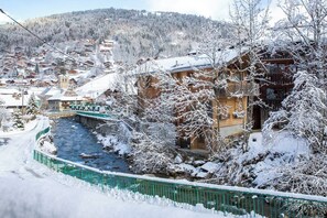 En snøklædt landsby med en flod, træhuse og en bro.