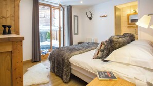A cozy bedroom with a large bed, a wooden dresser, a fireplace, and a view of the outside. - More Mountain - Apartment Central in the heart of Morzine with Outdoor Jacuzzi. Less than 5 minutes walk to ski lifts & bars. (Morzine)
