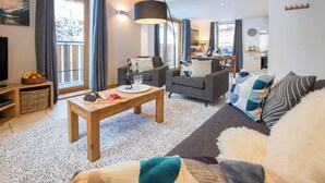 A modern living room with a wooden coffee table, grey sofas, and a large window with curtains. - More Mountain - Apartment Central in the heart of Morzine with Outdoor Jacuzzi. Less than 5 minutes walk to ski lifts & bars. (Morzine)