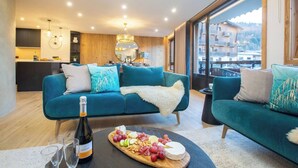 A modern living room with a teal sofa set, a wooden dining table with a cheese platter, and a bottle of wine. - More Mountain  - Demi Lune. Central Morzine location and less than 2 minutes walk to main ski lifts, bars and restaurants. (Morzine)