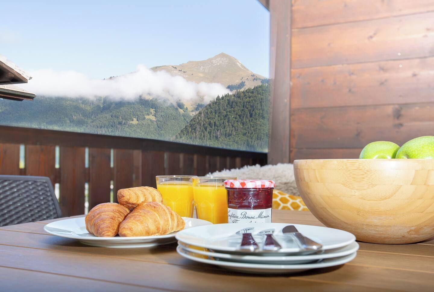 Ein Frühstückstisch mit Croissants, Orangensaft, Marmelade und einer Schüssel Äpfel.