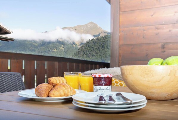A breakfast table with croissants, orange juice, jam, and a bowl of apples.