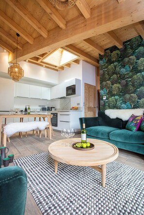 Ein modernes Wohnzimmer mit Holzboden, einem grünen Sofa, einem runden Couchtisch mit Obstschale und einem gemusterten Teppich.