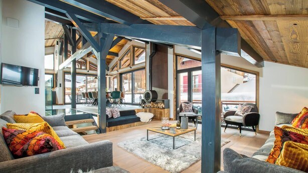 Amplia sala de estar con techo alto, vigas de madera y ventanas grandes que ofrecen vistas al exterior.