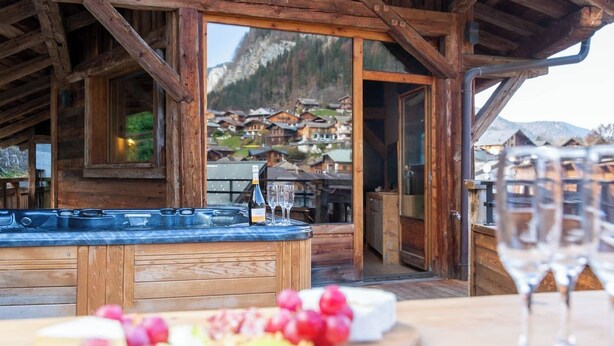 Una cabaña de madera con jacuzzi, una copa de champán y una bandeja de frutas.