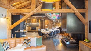 Un interior estilo loft espacioso con vigas de madera a la vista, un área de comedor central, una zona de estar acogedora y una cocina moderna.