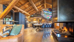 Amplia sala de estar con techo alto, chimenea y comedor con sillas modernas y una barra.