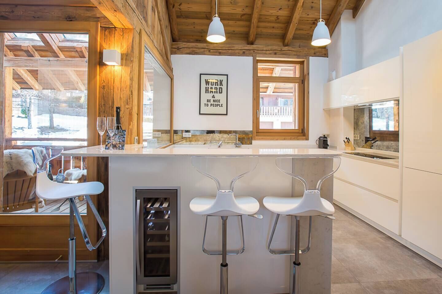 Une cuisine moderne avec un coin bar, des poutres apparentes en bois au plafond et une vue sur l’extérieur.