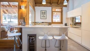 Une cuisine moderne avec un coin bar, des poutres apparentes en bois au plafond et une vue sur l’extérieur.