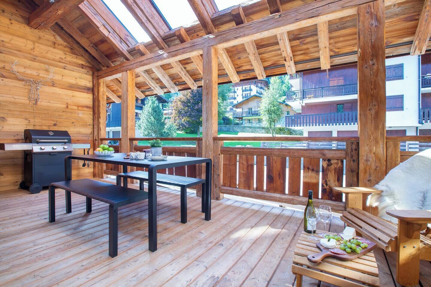 Une terrasse en bois avec un barbecue, une table et des bancs.