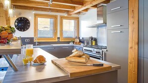 A modern kitchen with a central island, wooden beams, a large clock, and a view of the outdoors. - More Mountain - Chalet Jirishanca in central Morzine with Outdoor Jacuzzi. Large split level chalet less than 2 minutes walk to ski lifts & bars. (Morzine)