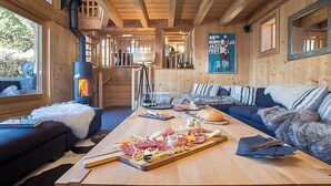 A cozy cabin interior with a wooden interior, a fireplace, a dining area with a charcuterie board, and a sofa. - More Mountain - Chalet Jirishanca in central Morzine with Outdoor Jacuzzi. Large split level chalet less than 2 minutes walk to ski lifts & bars. (Morzine)