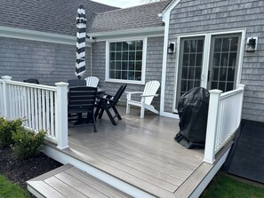 En overdækket terrasse med et bord, stole, grill og gelænder i hvid.