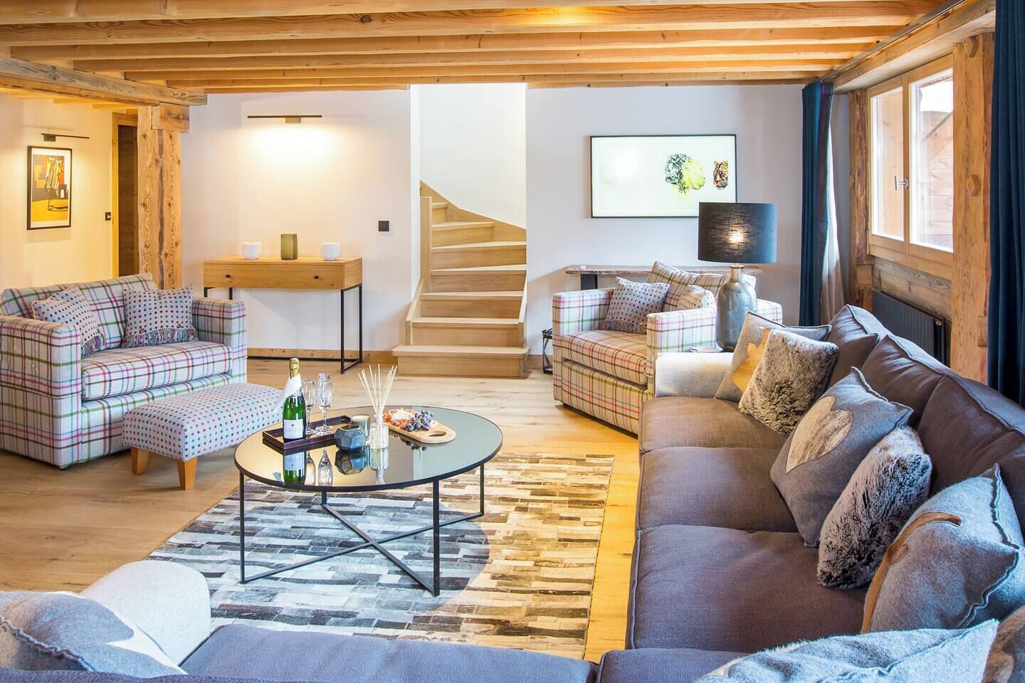 Una sala de estar acogedora con sofás a cuadros, una mesa de centro y una escalera que sube a otro nivel.