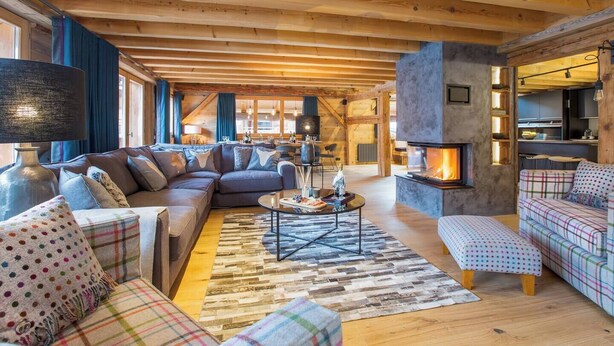 A cozy living room with a fireplace, wooden beams, and a large sofa.