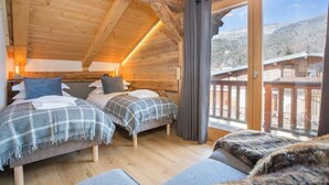 A cozy cabin room with two beds, wooden walls, and a balcony with a view of the mountains.