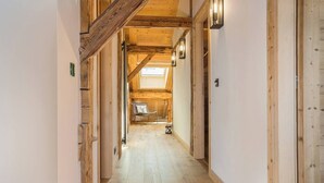 A wooden interior hallway with a sloped ceiling and skylight, leading to a room with a chair and a small table.