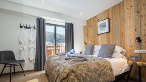 A modern bedroom with a large bed, wooden panel walls, a view of a snowy landscape, a chair, and a fluffy rug. - More Mountain - Chalet La Godille. Luxury Chalet with large Terrace and Outdoor Jacuzzi split over 3 levels next to the Super Morzine Telecabine. (Morzine)
